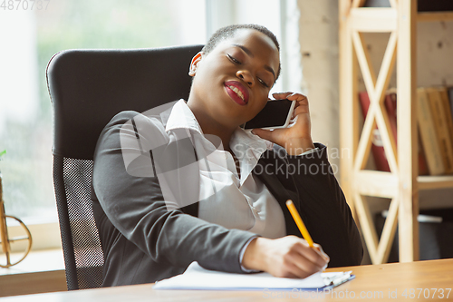 Image of African-american businesswoman in office attire smiling, looks confident and happy, successful