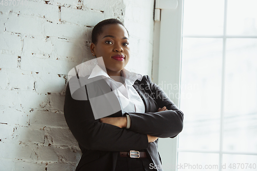 Image of African-american businesswoman in office attire smiling, looks confident and happy, successful