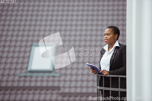 Image of African-american businesswoman in office attire smiling, looks confident and happy, successful