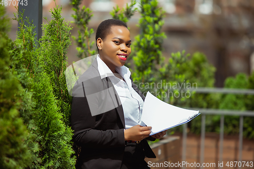 Image of African-american businesswoman in office attire smiling, looks confident and happy, successful