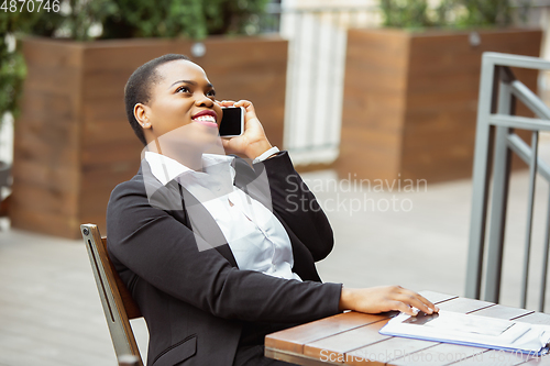 Image of African-american businesswoman in office attire smiling, looks confident and happy, successful