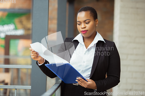 Image of African-american businesswoman in office attire smiling, looks confident and happy, successful