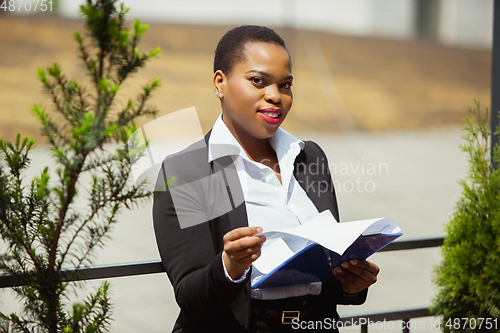 Image of African-american businesswoman in office attire smiling, looks confident and happy, successful