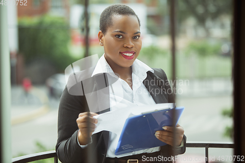 Image of African-american businesswoman in office attire smiling, looks confident and happy, successful