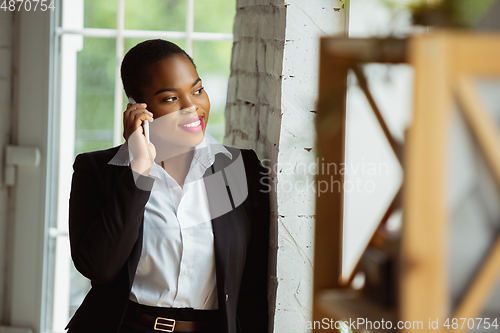 Image of African-american businesswoman in office attire smiling, looks confident and happy, successful