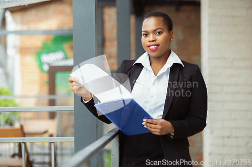 Image of African-american businesswoman in office attire smiling, looks confident and happy, successful