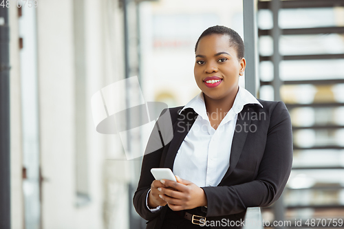 Image of African-american businesswoman in office attire smiling, looks confident and happy, successful