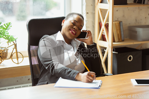 Image of African-american businesswoman in office attire smiling, looks confident and happy, successful