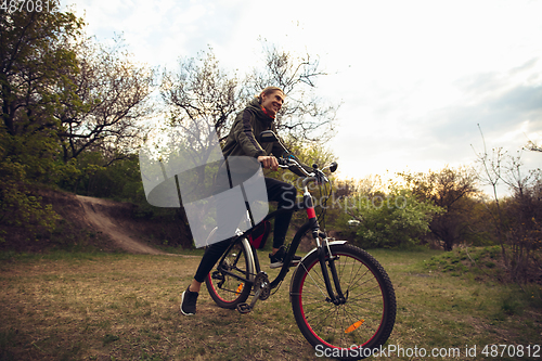 Image of Young man having fun near countryside park, riding bike, traveling at spring day