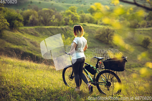 Image of Young woman having fun near countryside park, riding bike, traveling at spring day