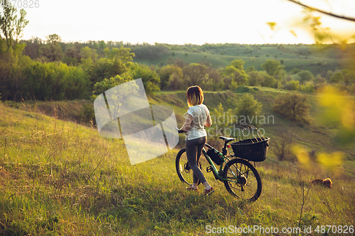 Image of Young woman having fun near countryside park, riding bike, traveling with companion spaniel dog