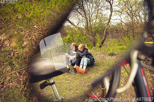 Image of Best friends having fun near countryside park, resting after riding bikes, spending time together, sitting on the grass. Reflection in mirror.