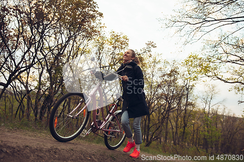 Image of Young woman having fun near countryside park, riding bike, traveling at spring day