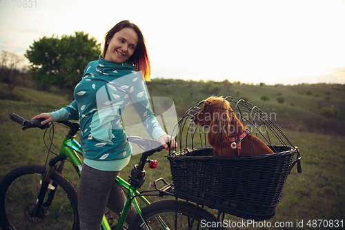 Image of Young woman having fun near countryside park, riding bike, traveling with companion spaniel dog