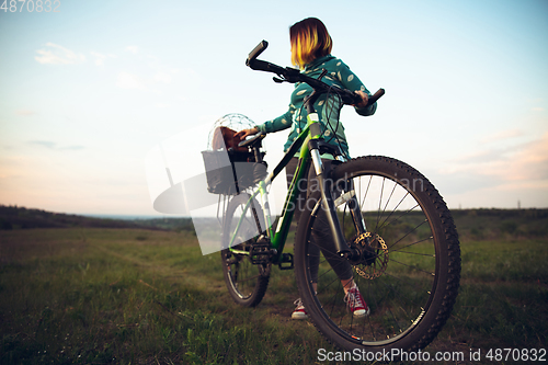 Image of Young woman having fun near countryside park, riding bike, traveling with companion spaniel dog