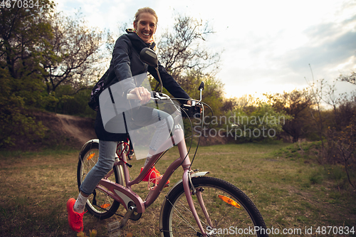 Image of Young woman having fun near countryside park, riding bike, traveling at spring day