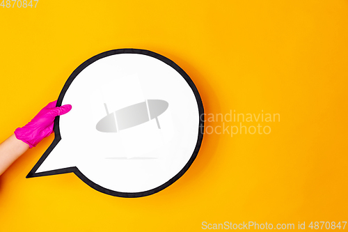 Image of Hand in pink rubber glove holding comment isolated on yellow studio background with copyspace.