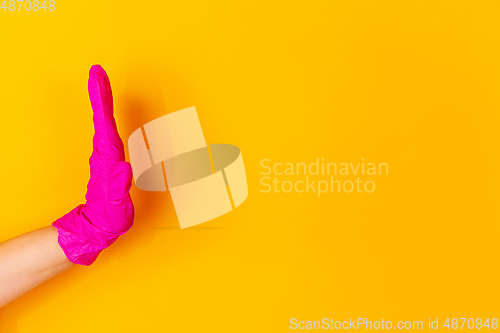 Image of Hand in pink rubber glove greeting, waving isolated on yellow studio background with copyspace.