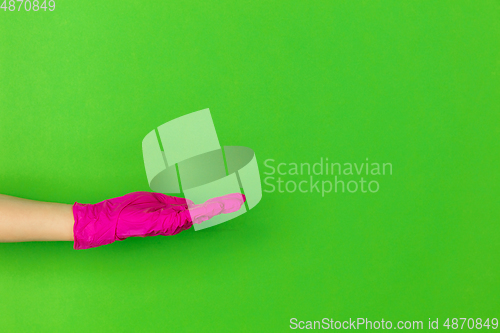 Image of Hand in pink rubber glove showing, presenting isolated on green studio background with copyspace.