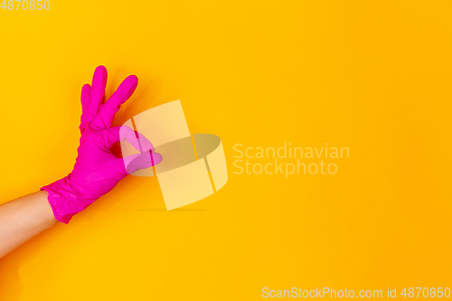 Image of Hand in pink rubber glove showing nice sign isolated on yellow studio background with copyspace.
