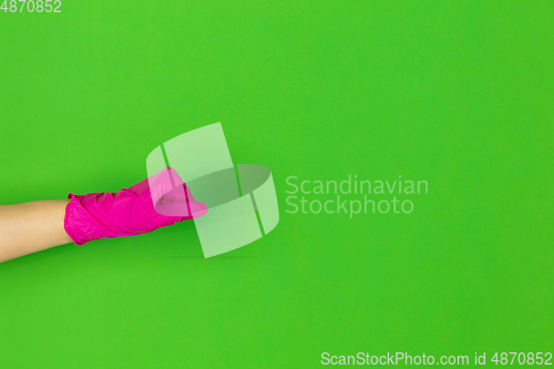 Image of Hand in pink rubber glove shows fist bump isolated on green studio background with copyspace.