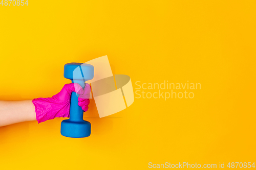 Image of Hand in pink rubber glove holding dumbbell, gym weight isolated on yellow studio background with copyspace.