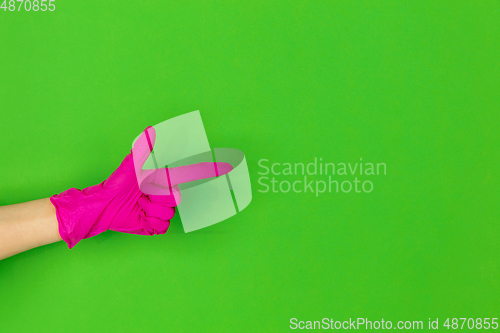 Image of Hand in pink rubber glove pointing isolated on green studio background with copyspace.