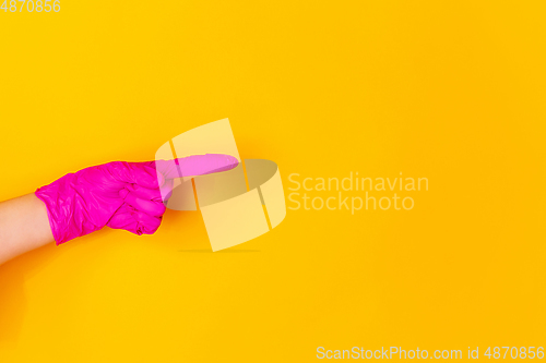 Image of Hand in pink rubber glove pointing isolated on yellow studio background with copyspace.