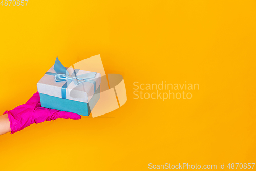 Image of Hand in pink rubber glove holding gift isolated on yellow studio background with copyspace.