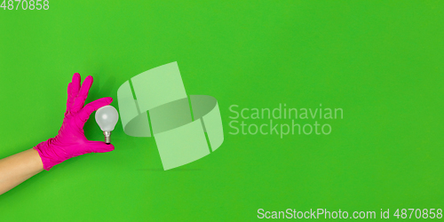 Image of Hand in pink rubber glove with lightbulb isolated on green studio background with copyspace. Flyer, proposal.