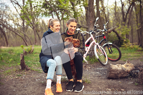 Image of Best friends having fun near countryside park, resting after riding bikes, spending time together, sitting on the grass