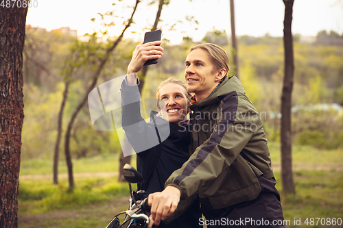 Image of Best friends having fun near countryside park, resting after riding bikes, spending time together, sitting on the grass. Taking selfie.