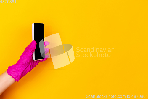 Image of Hand in pink rubber glove holding smartphone with blank screen isolated on yellow studio background with copyspace.