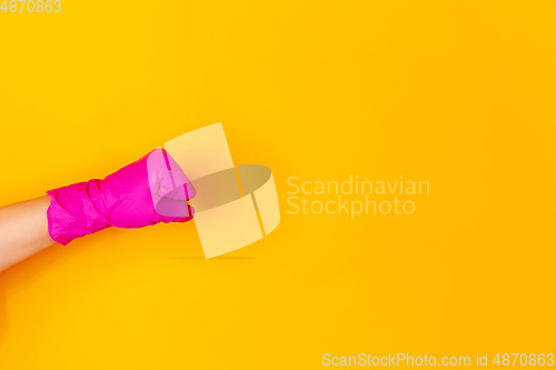 Image of Hand in pink rubber glove showing fist bump isolated on yellow studio background with copyspace.