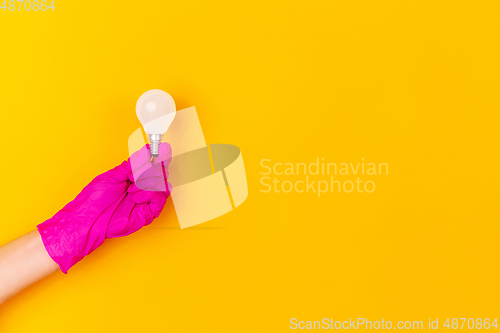 Image of Hand in pink rubber glove holding lightbulb isolated on yellow studio background with copyspace.