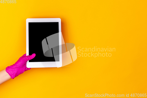 Image of Hand in pink rubber glove holding tablet with blank screen isolated on yellow studio background with copyspace.