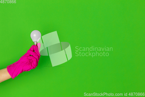 Image of Hand in pink rubber glove with lightbulb isolated on green studio background with copyspace.