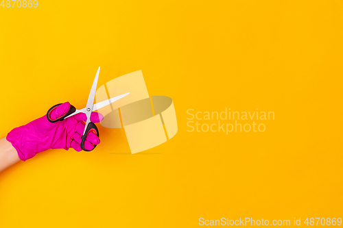 Image of Hand in pink rubber glove holding sccissors isolated on yellow studio background with copyspace.