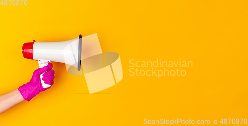 Image of Hand in pink rubber glove holding megaphone isolated on yellow studio background with copyspace. Flyer.