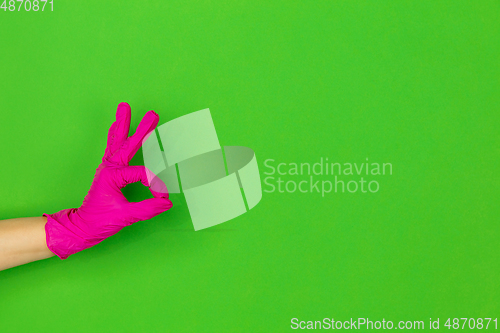 Image of Hand in pink rubber glove showing nice sign isolated on green studio background with copyspace.