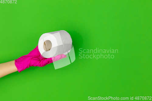 Image of Hand in pink rubber glove with toilet paper isolated on green studio background with copyspace.