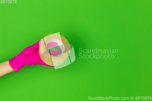 Image of Hand in pink rubber glove with skotch tape isolated on green studio background with copyspace.