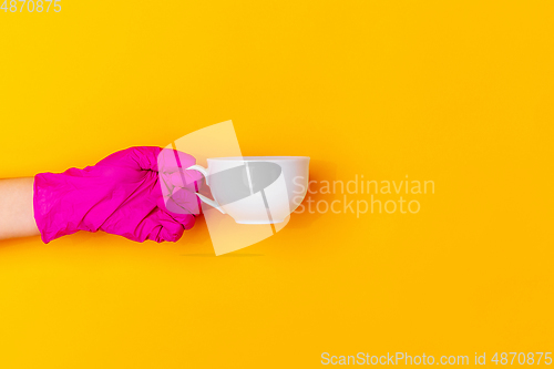 Image of Hand in pink rubber glove holding coffee cup isolated on yellow studio background with copyspace.
