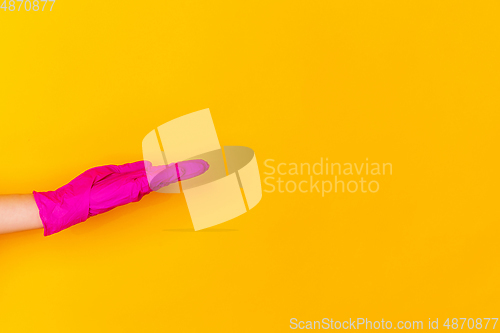 Image of Hand in pink rubber glove taking, showing isolated on yellow studio background with copyspace.