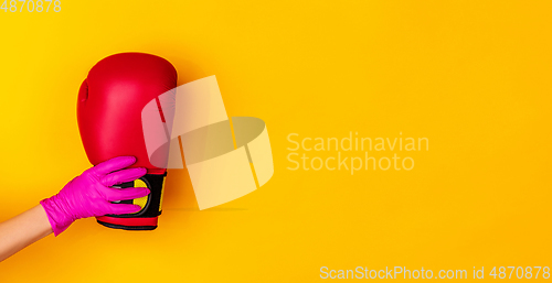 Image of Hand in pink rubber glove holding boxer\'s glove isolated on yellow studio background with copyspace. Flyer.