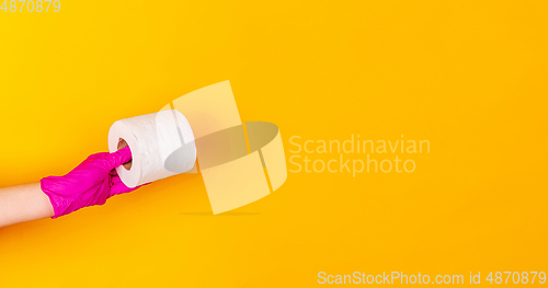 Image of Hand in pink rubber glove holding toilet paper isolated on yellow studio background with copyspace. Flyer.