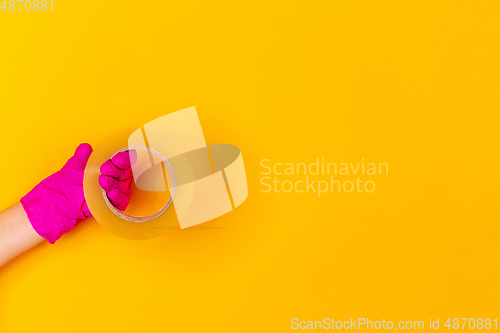 Image of Hand in pink rubber glove holding skotch tape isolated on yellow studio background with copyspace.