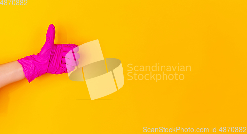 Image of Hand in pink rubber glove showing thumb up isolated on yellow studio background with copyspace. flyer.