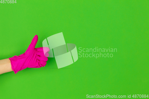 Image of Hand in pink rubber glove showing thumb up isolated on green studio background with copyspace.