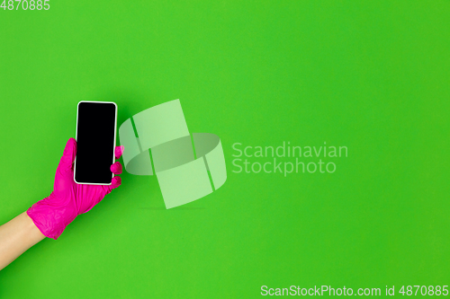 Image of Hand in pink rubber glove holding smartphone isolated on green studio background with copyspace.